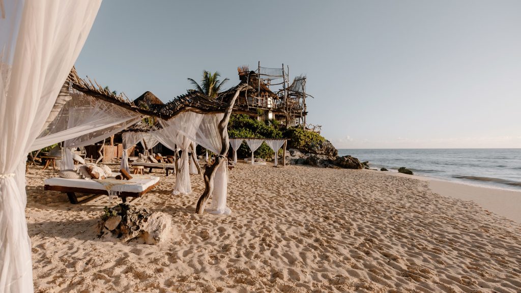 Azulik Tulum private Caribbean beach with thatched palapa shelters and hammocks strung between palm trees — no loungers, no crowds